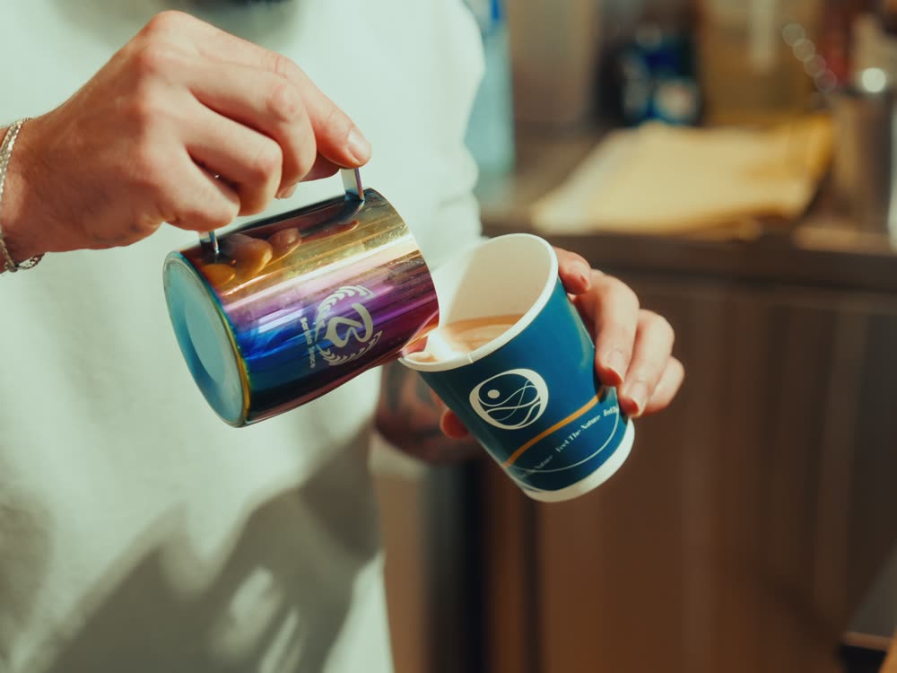 Barista pouring milk into a custom-printed paper cup